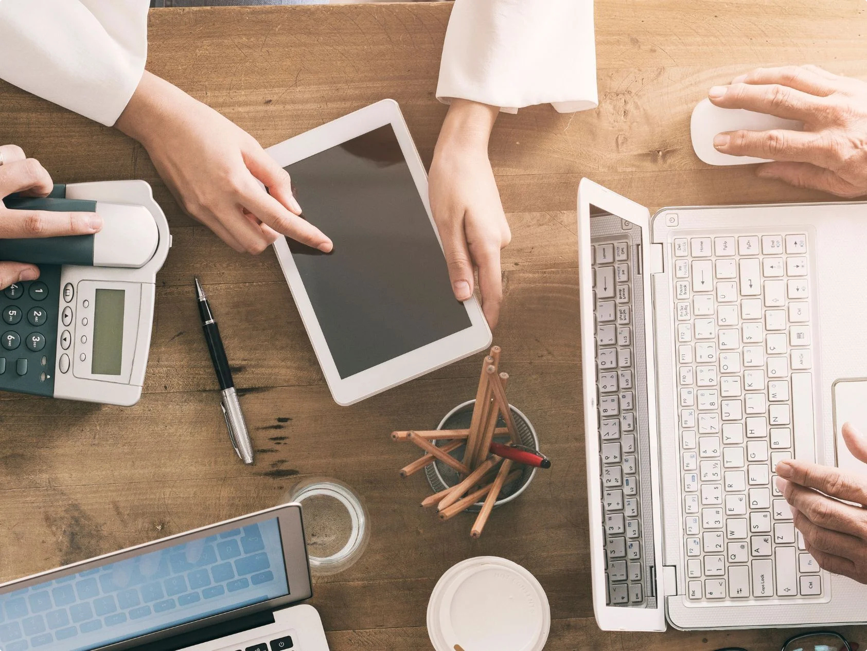 Hands working at a desk with a tablet, keyboard, calculator, and office supplies, representing digital waste management workflows.